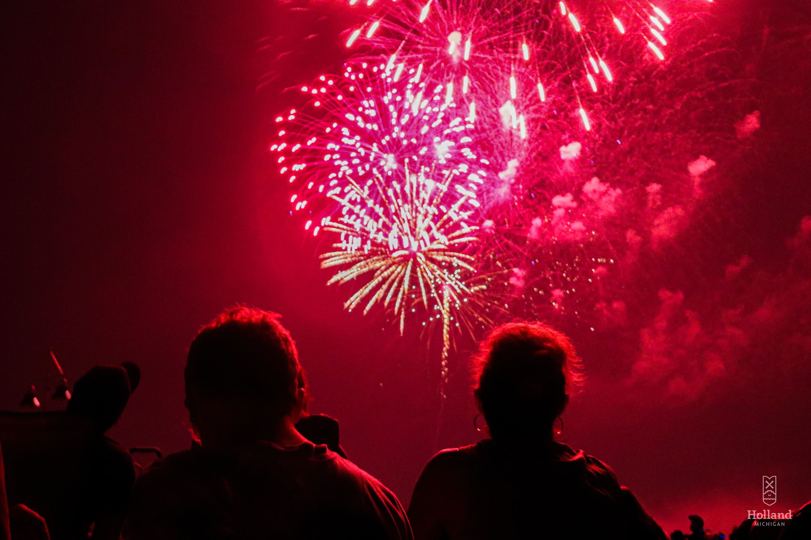 Red colored fireworks with head and shoulders of man and woman watching 