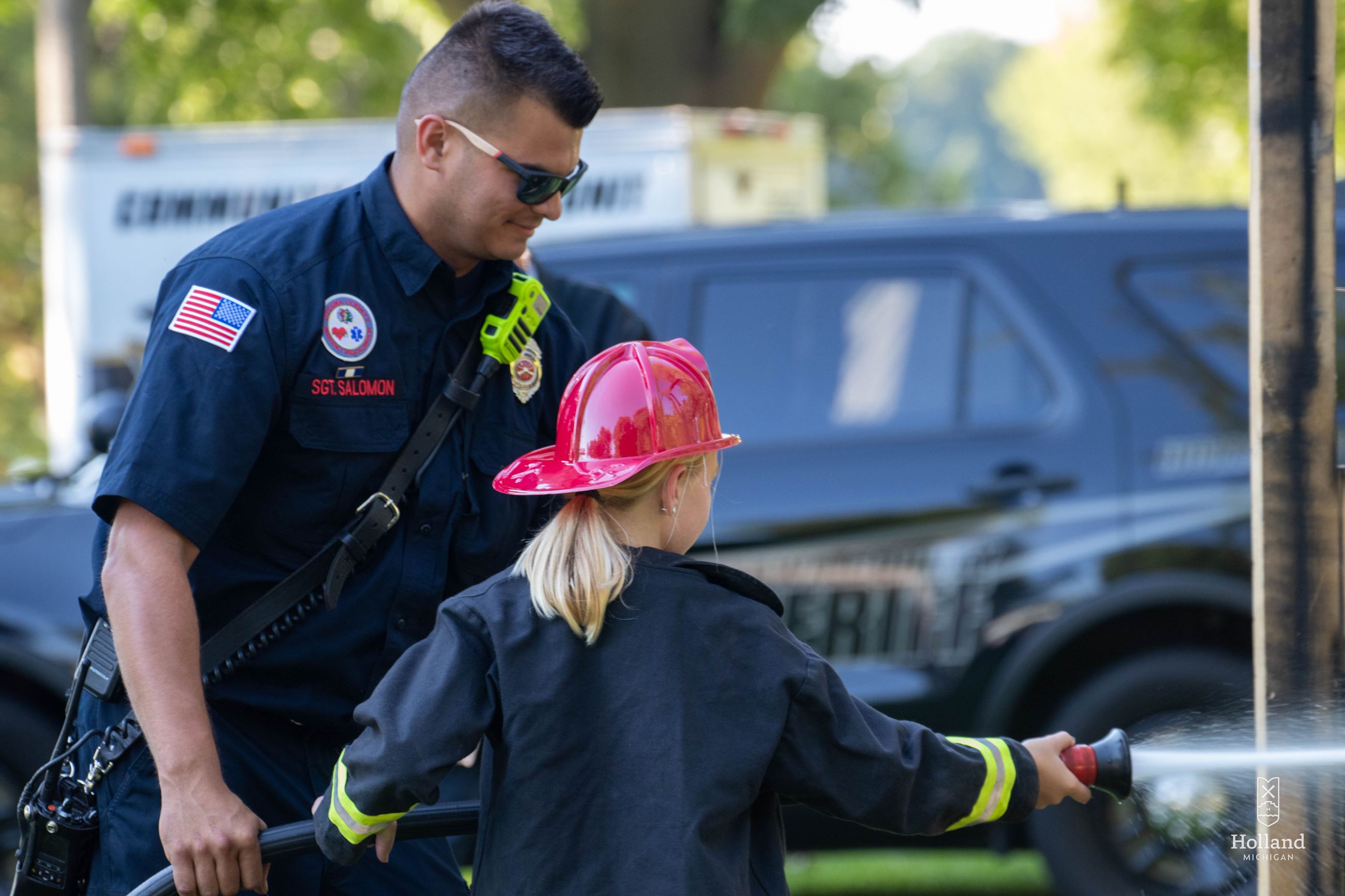 Male Firefighter assisting young girl with spraying a firehouse
