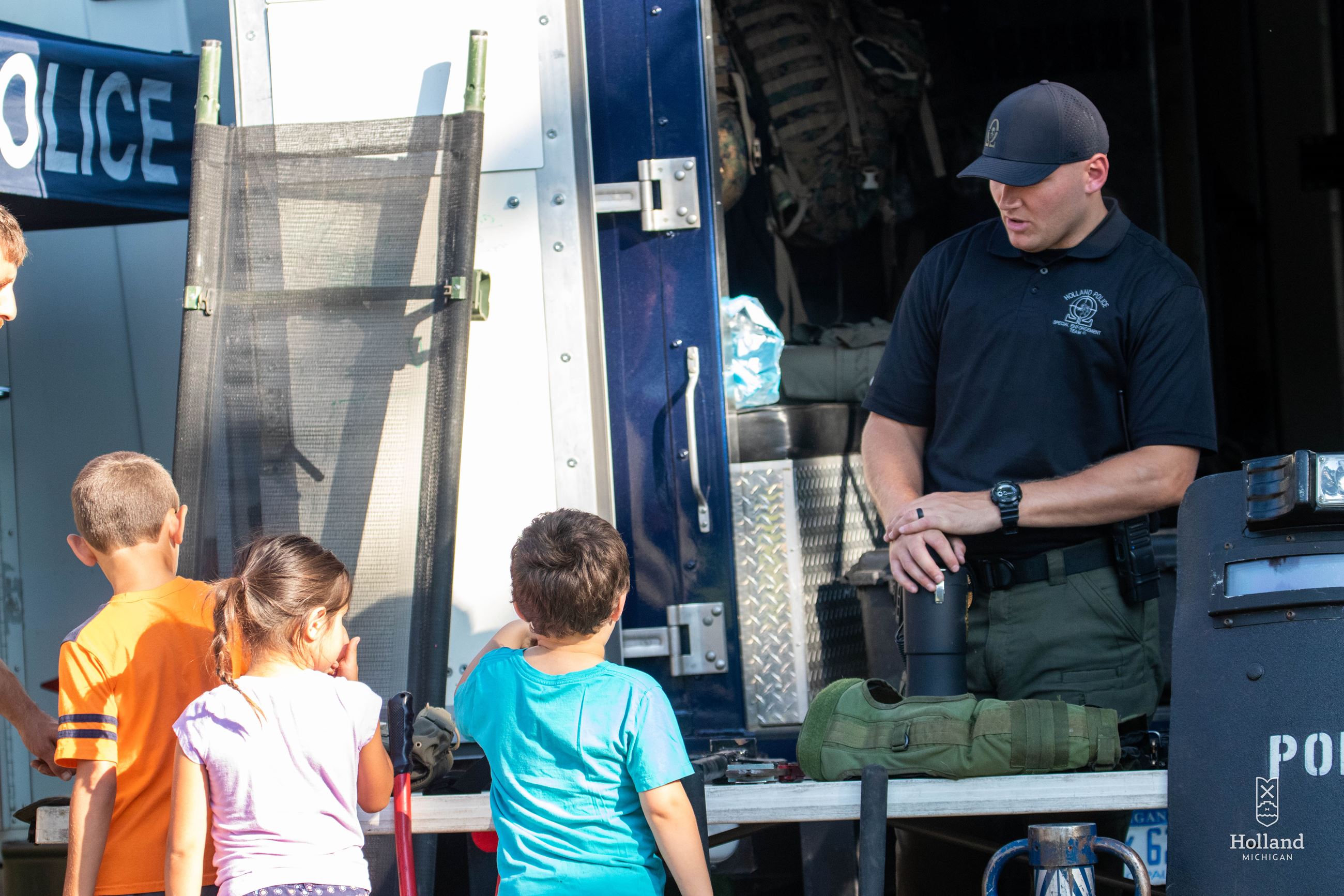 Police Officer talking with 3 young children at a booth displaying police equipment