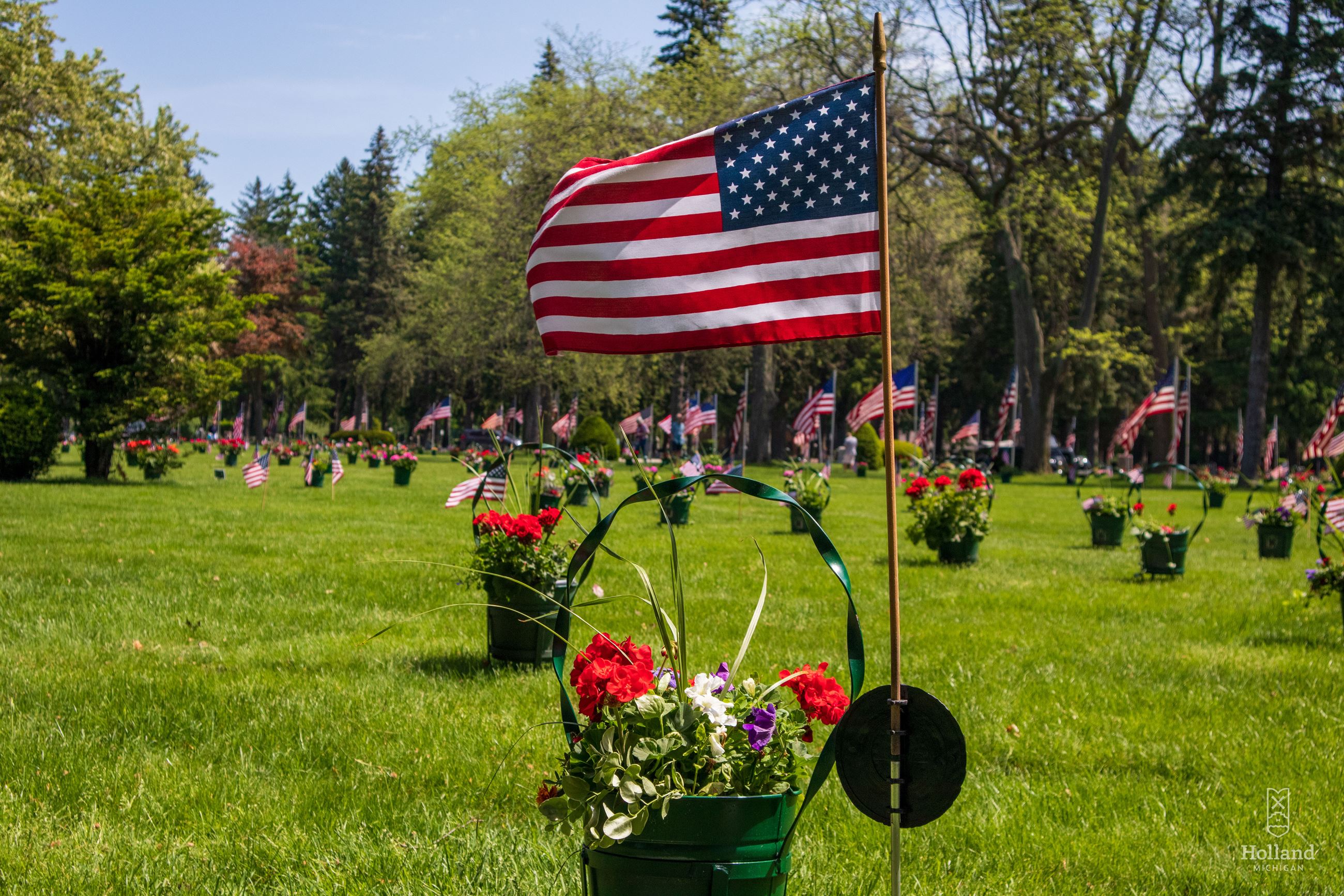 Cemetery Planter with red geraniums and small American Flag in the ground next to the planter