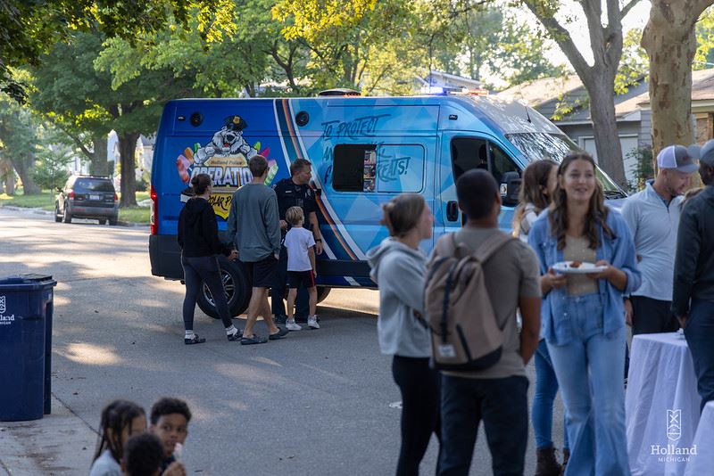 Neighbors gathered in the street talking with one another with an ice cream truck in the foreground.