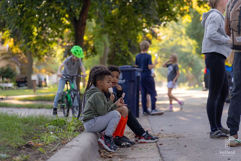 Three children sitting on the curb eating ice cream.
