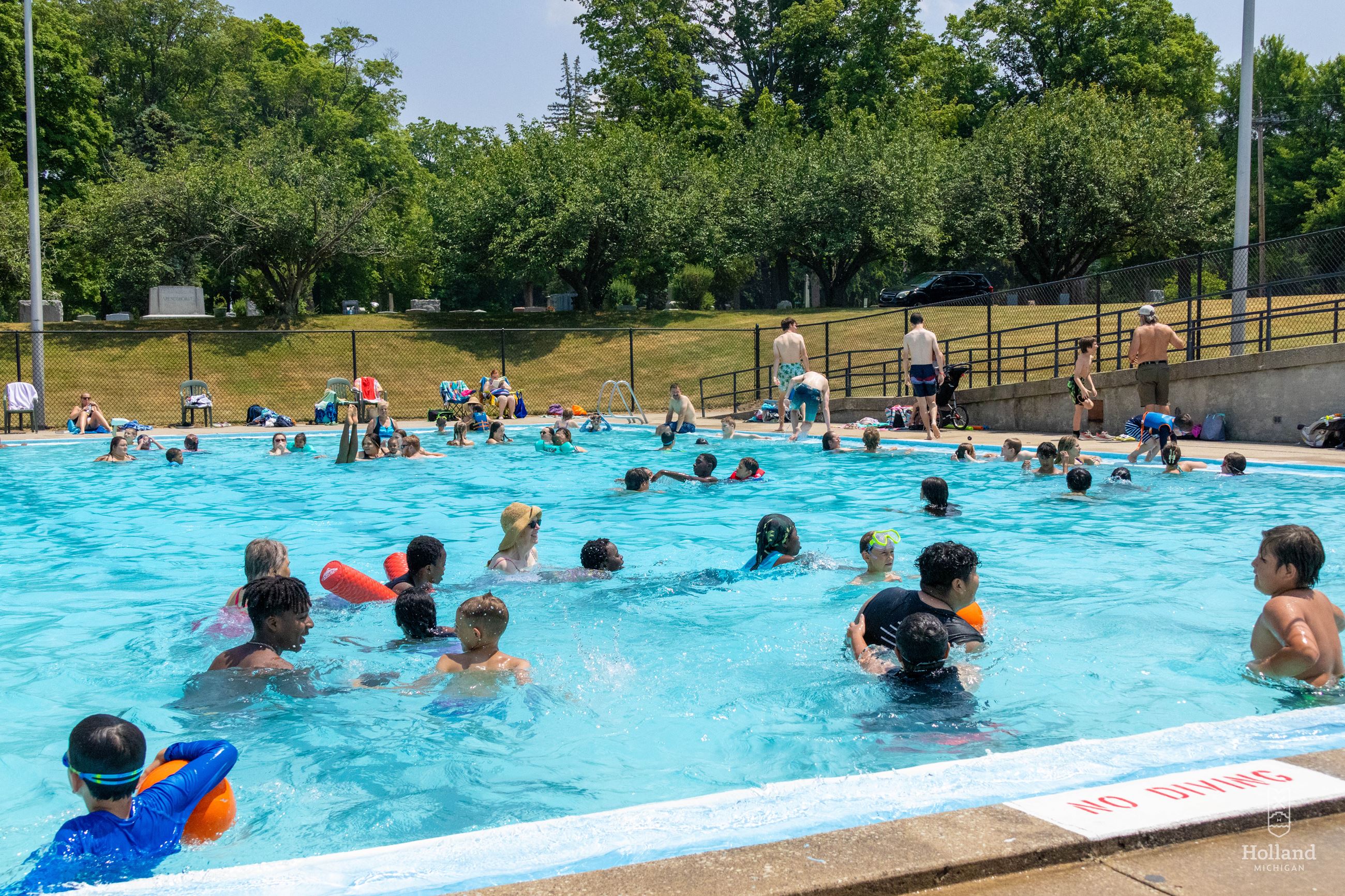Outdoor swimming pool with many people of various ages playing in the water