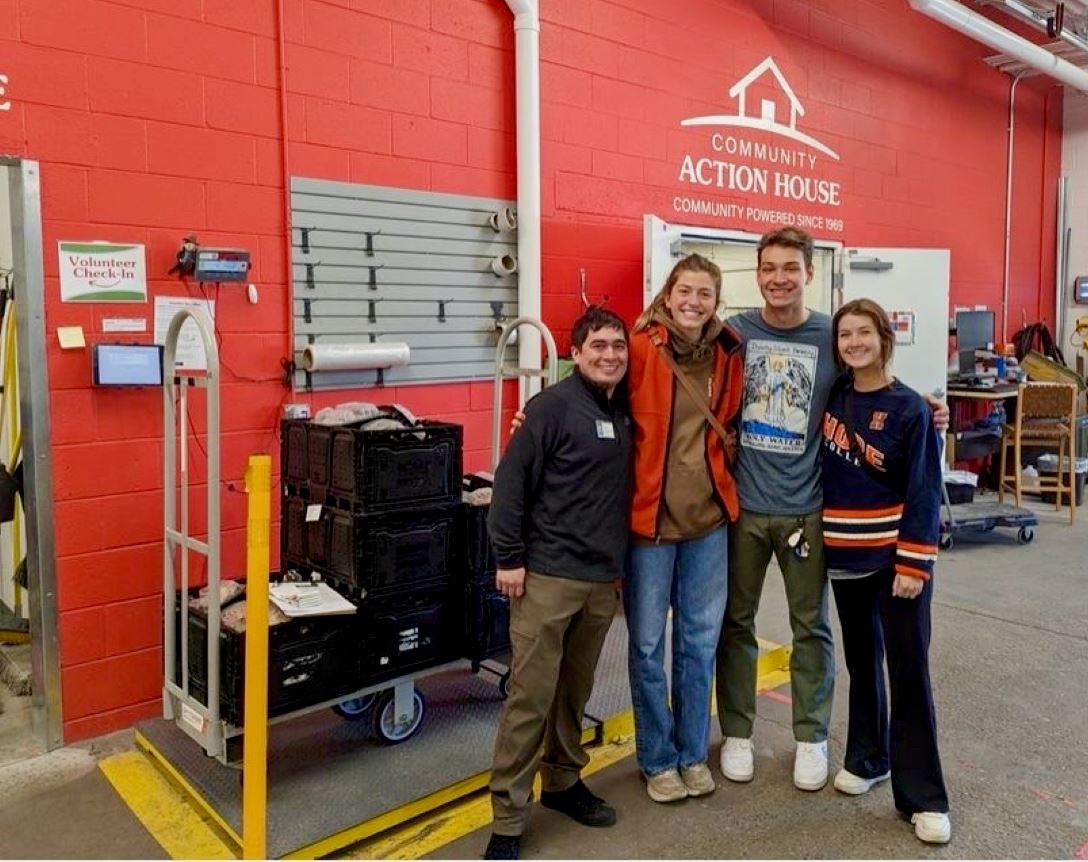 4 college students standing next to each other in a warehouse with pallets of food