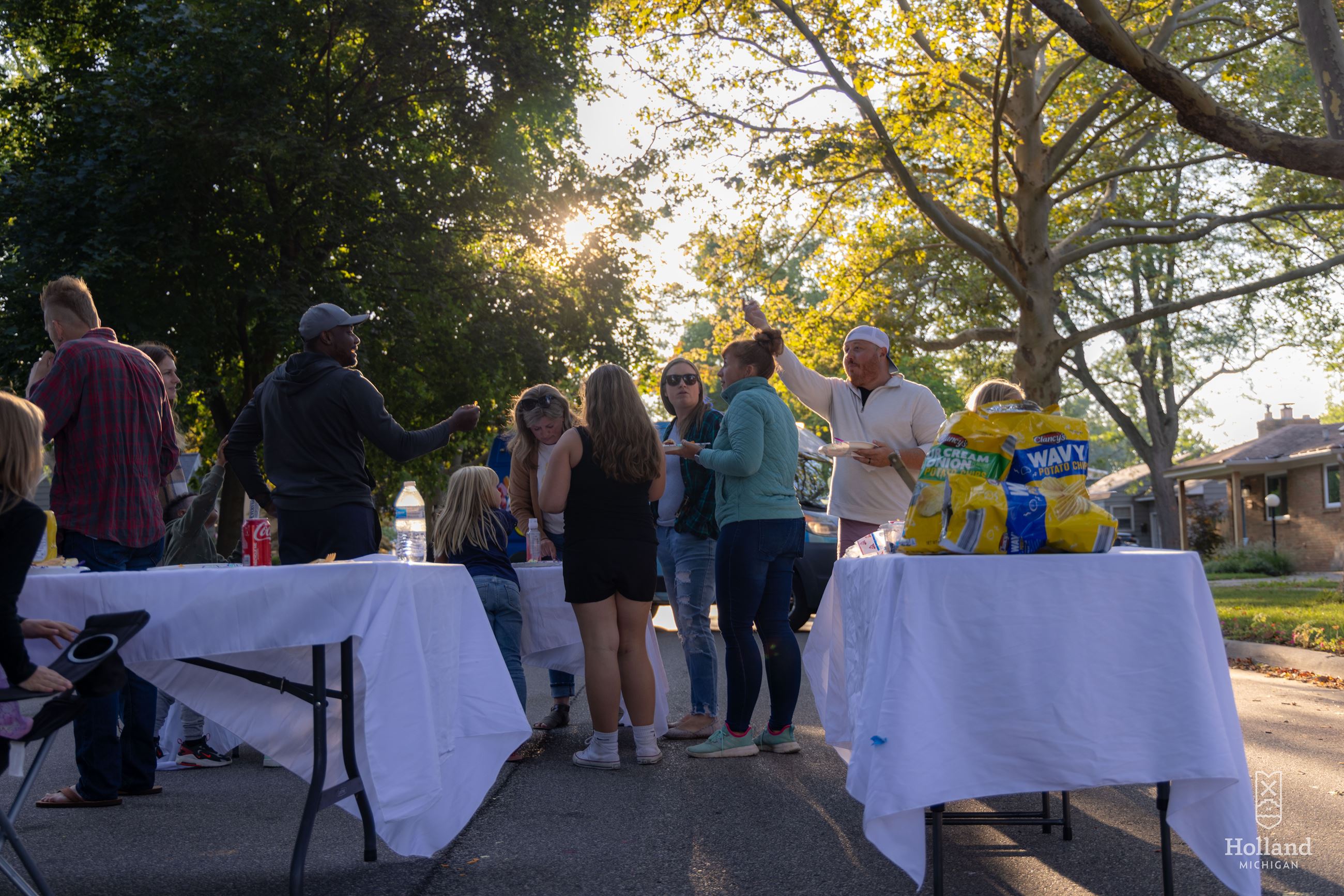 Neighbors gathered in a residential street for a block party. Table with food in forground