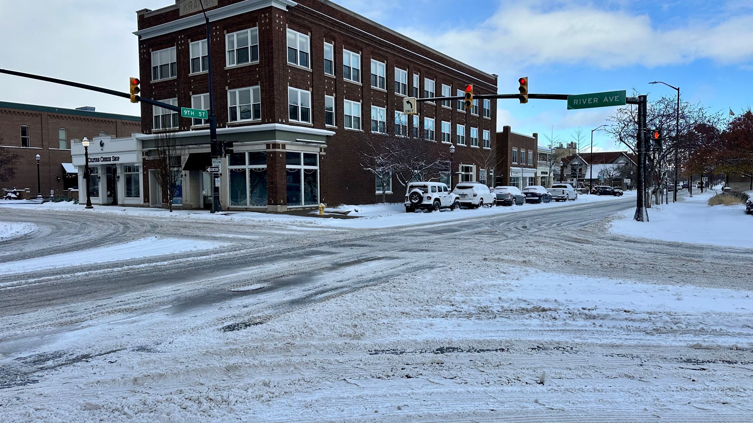 Snow and slush covered street intersection with a 4-story brown brick building on the corner