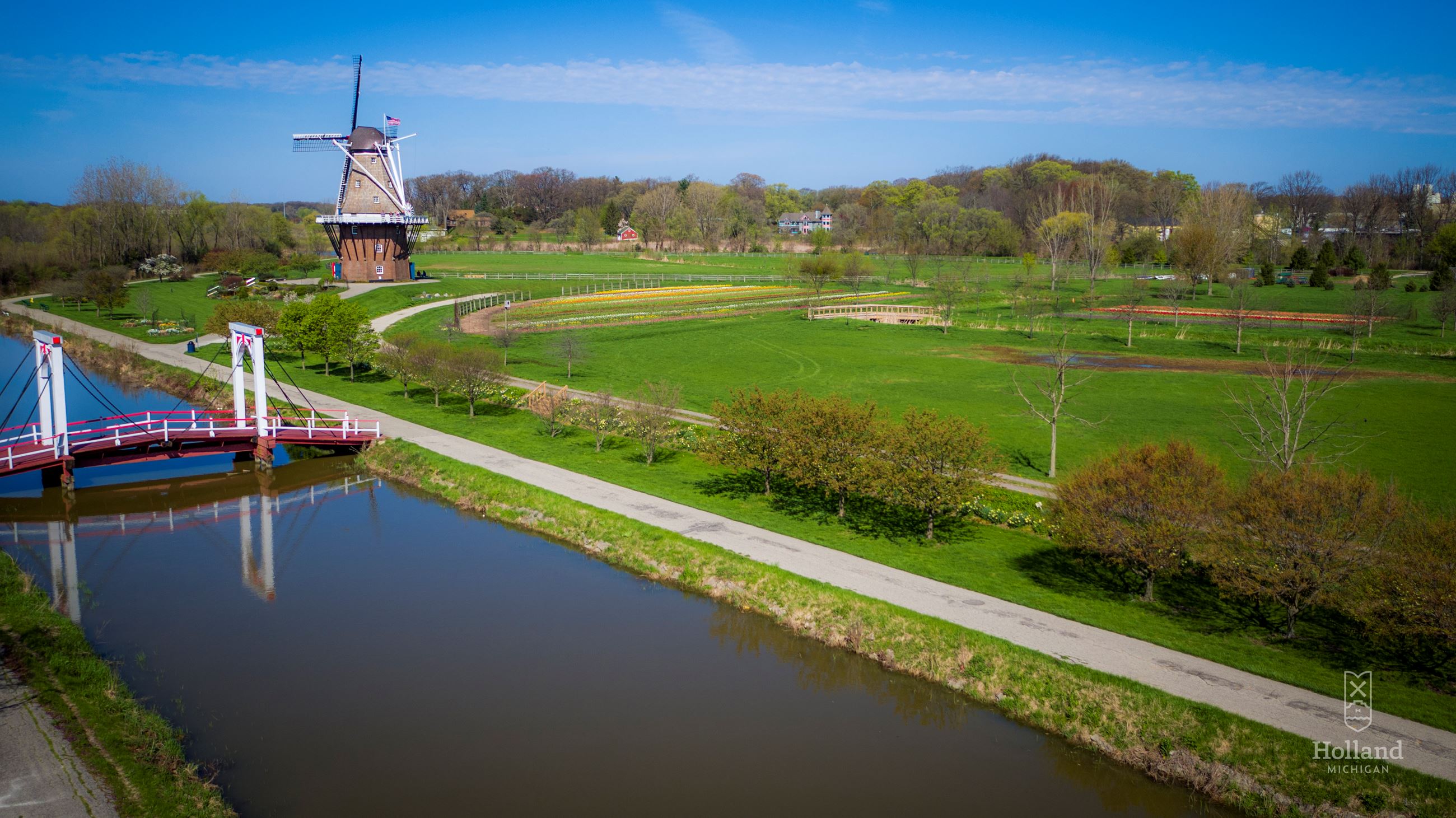 overhead view of a park, with a Dutch windmill in background, green grass and canal in front