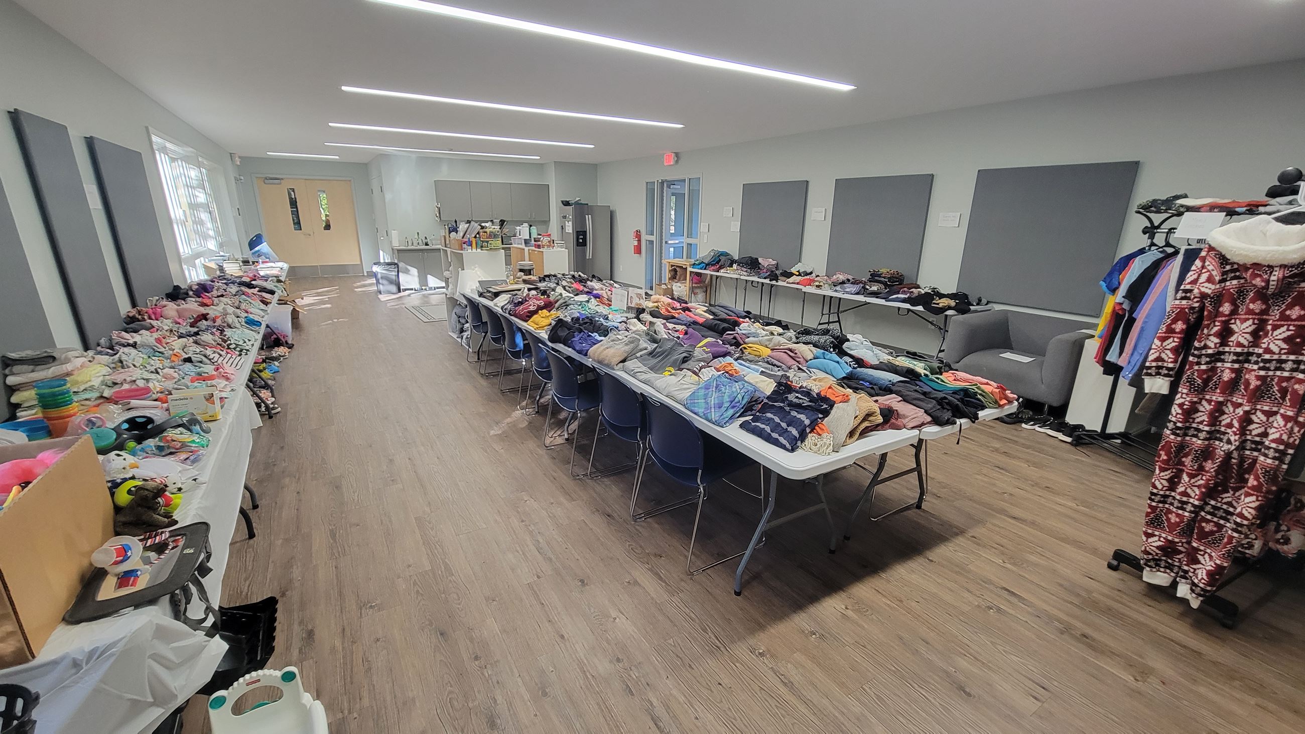 Large public room with long table filled with used clothing folded in neat piles