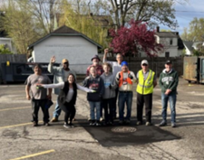 A group of people volunteering for a neighborhood cleanup event posing in a parking lot. 